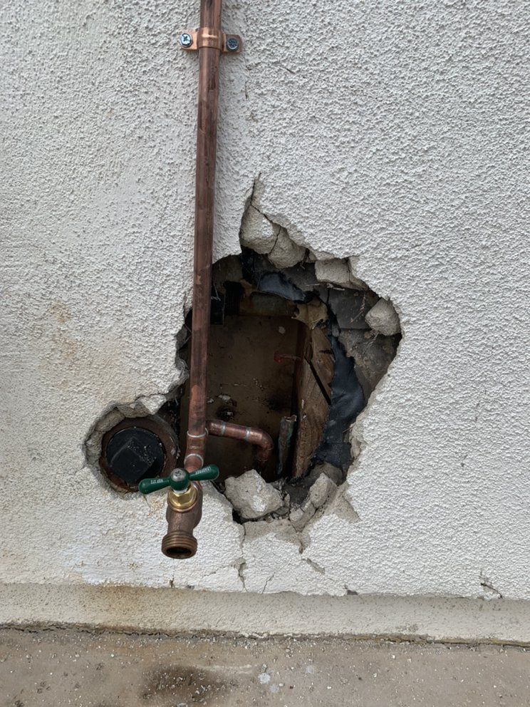 Damaged exterior wall with exposed plumbing pipes and a large hole in the stucco