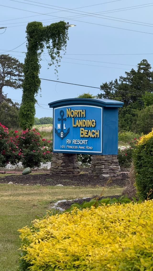Blue sign for a beach entrance beside landscaped greenery under a clear sky.