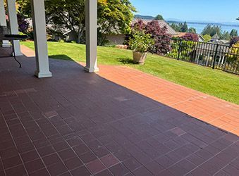Covered patio with dark tile floor, white columns, red brick border, and a green garden view.
