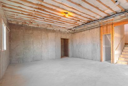 Unfinished concrete basement with exposed ceiling joists, doorway, and stairs on the right.