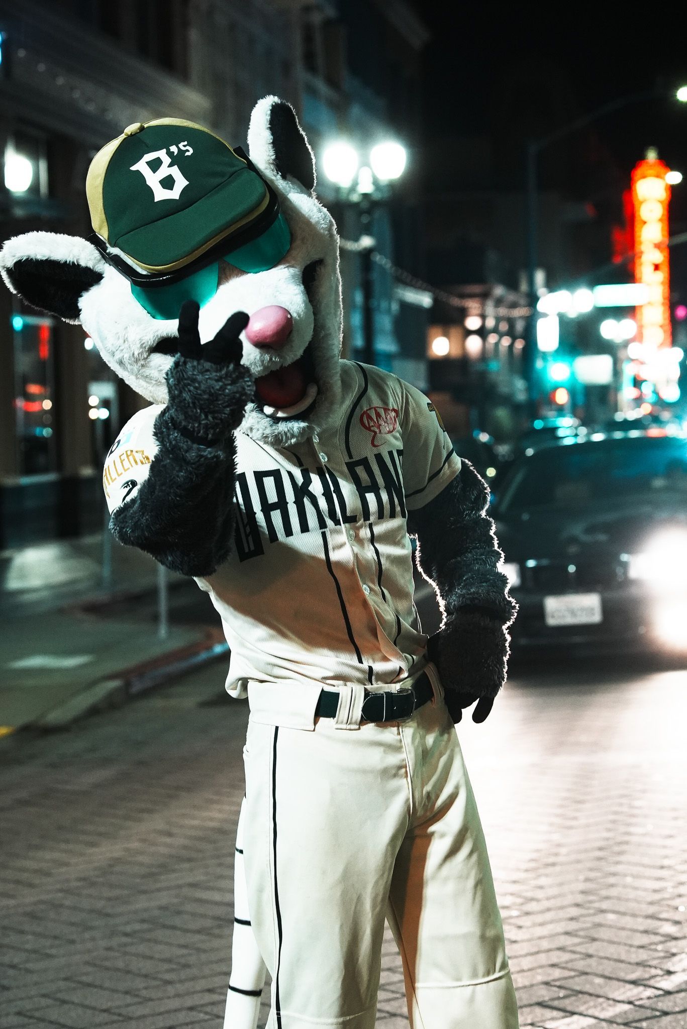 Person in a green cap and striped shirt poses on a city street at night.