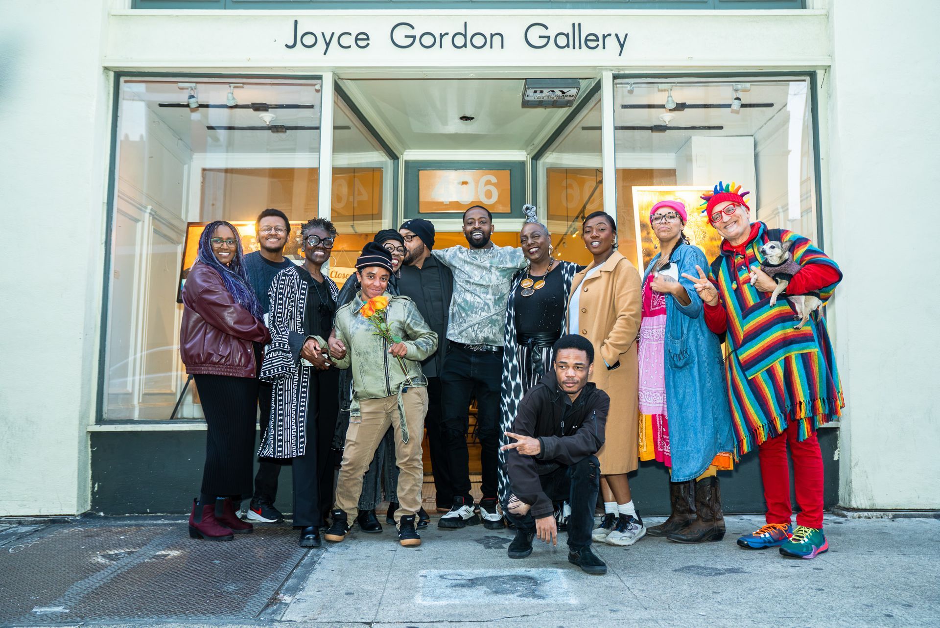 Group posing outside Joyce Gordon Gallery, with one person kneeling in front and colorful outfits on the right