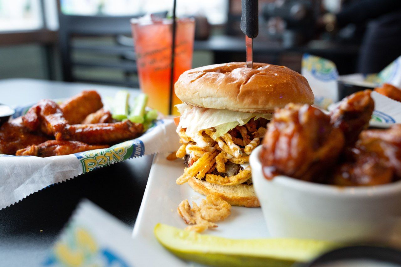 Plate of fried chicken and a sandwich with fries on a restaurant table, with a drink in the background
