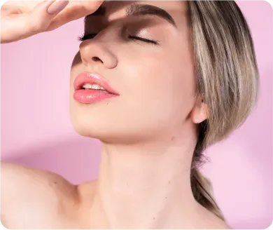 Woman shielding eyes from light, pink background, closed eyes, glossy lips.