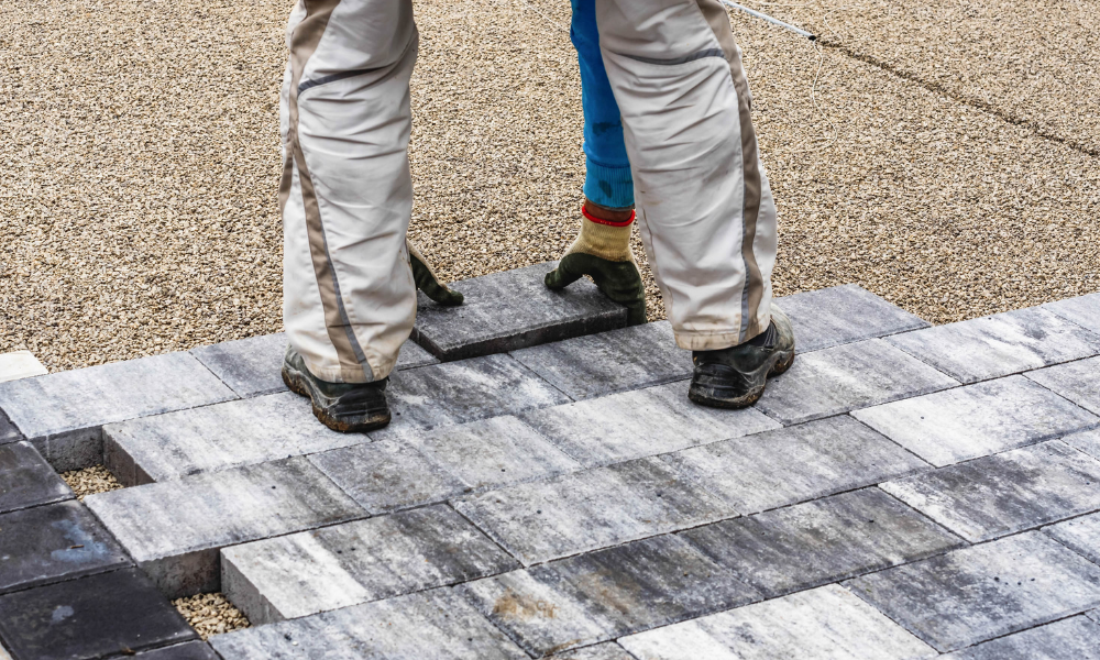 A man is laying bricks on a sidewalk.