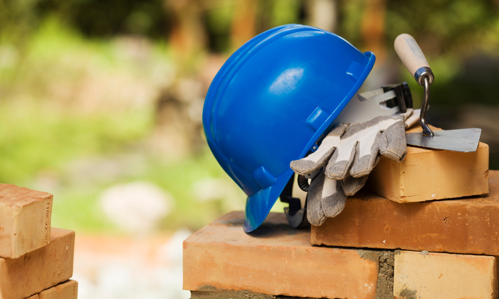 A blue hard hat , gloves , trowel and spatula are sitting on top of a brick wall.