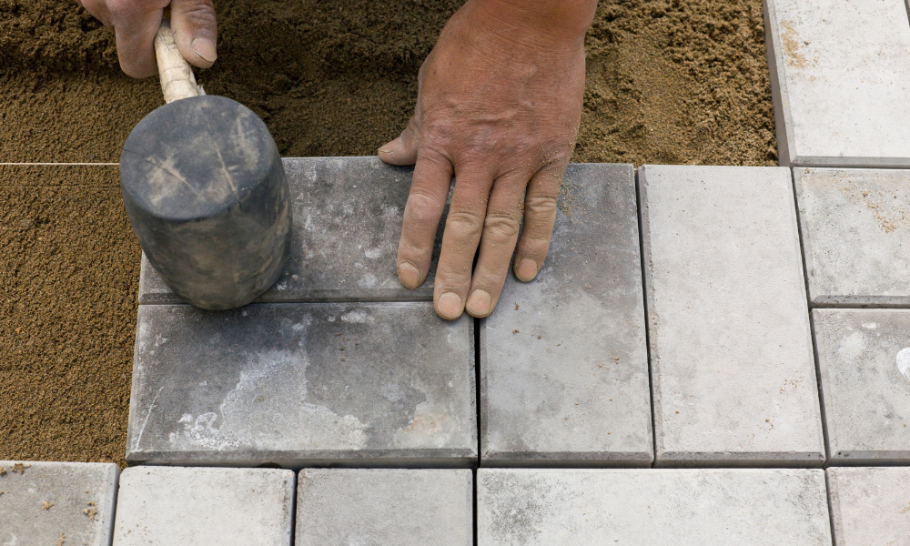 A man is laying bricks on a sidewalk with a rubber mallet.