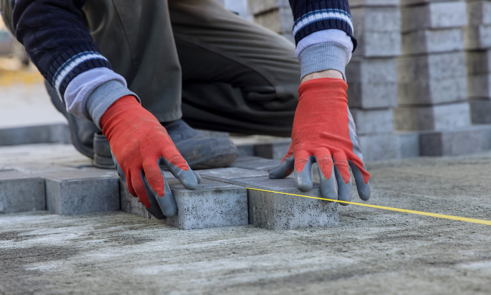 A man wearing red gloves is measuring bricks with a tape measure.