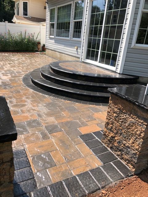 A patio with stairs and a stone wall in front of a house.