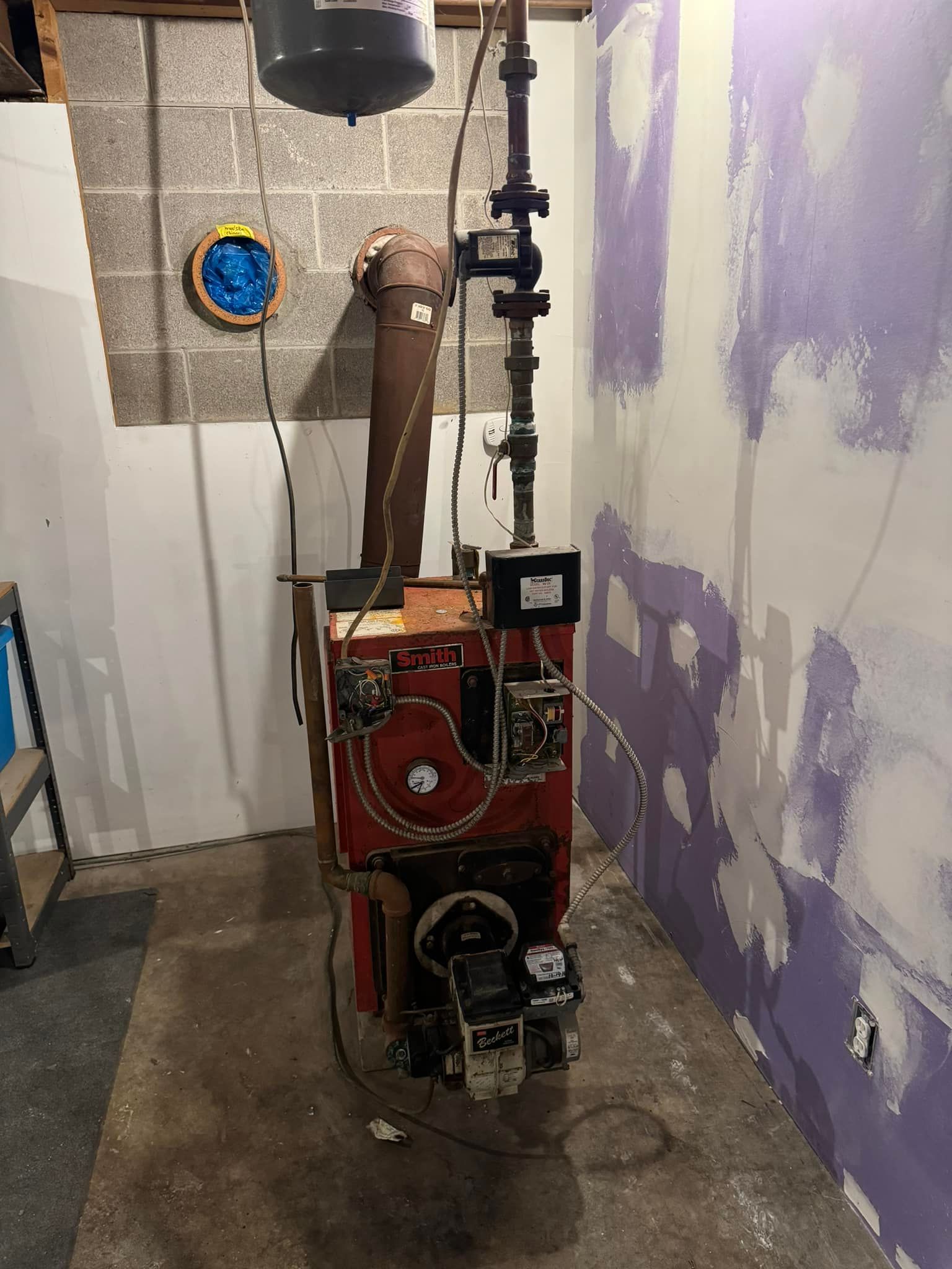 Red oil furnace in a basement setting, with exposed brick and partially painted walls.