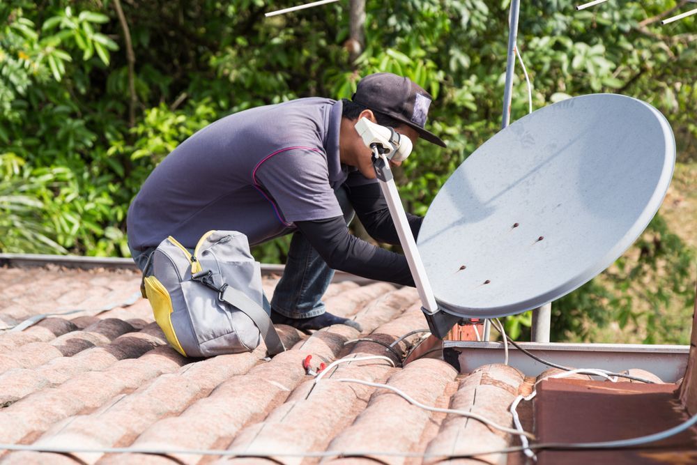 A Man is Working on a Satellite Dish on a Roof — Coffs Coast Antenna Services in Woolgoolga, NSW
