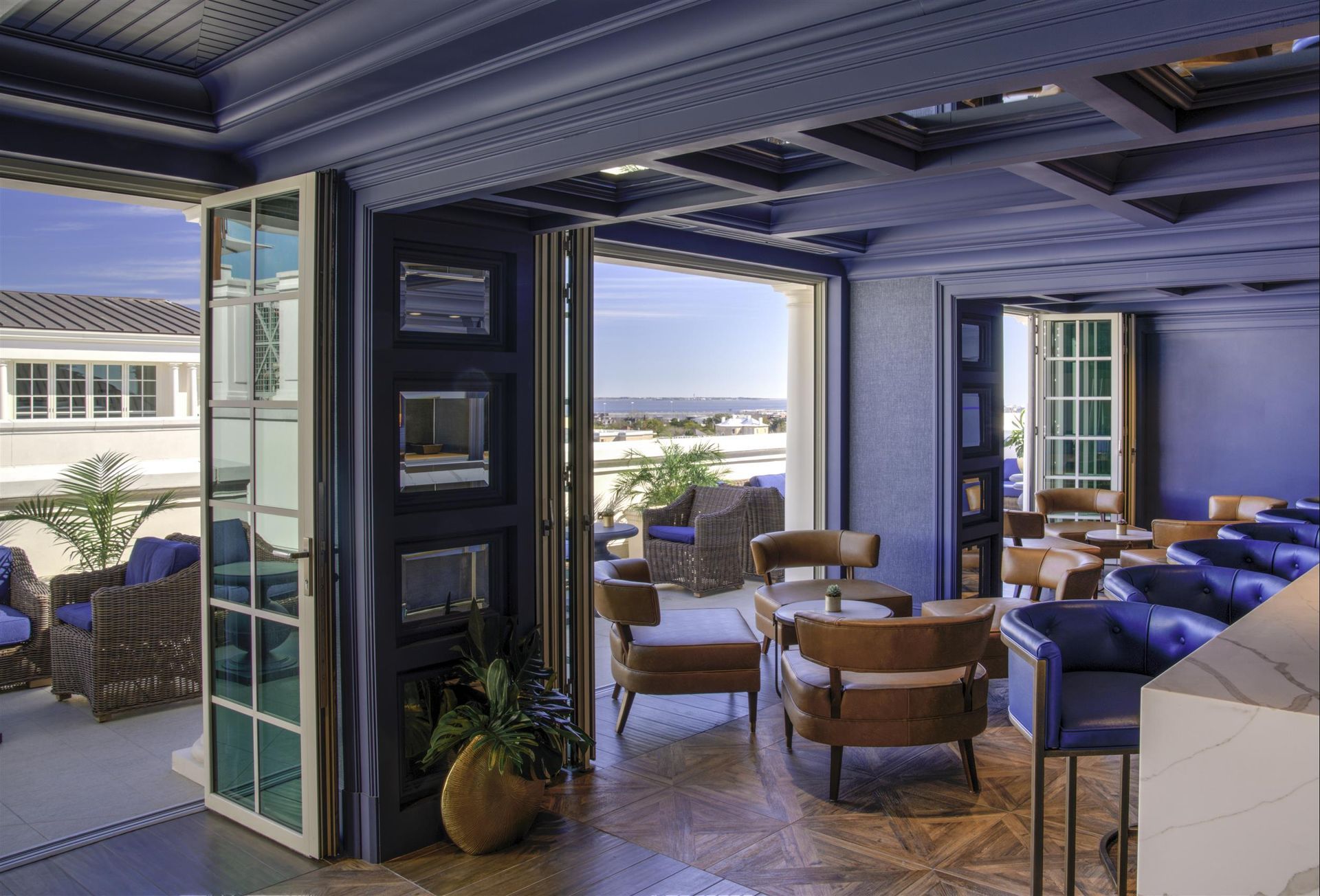 A room with a lot of chairs and tables and a balcony with a view of the ocean.