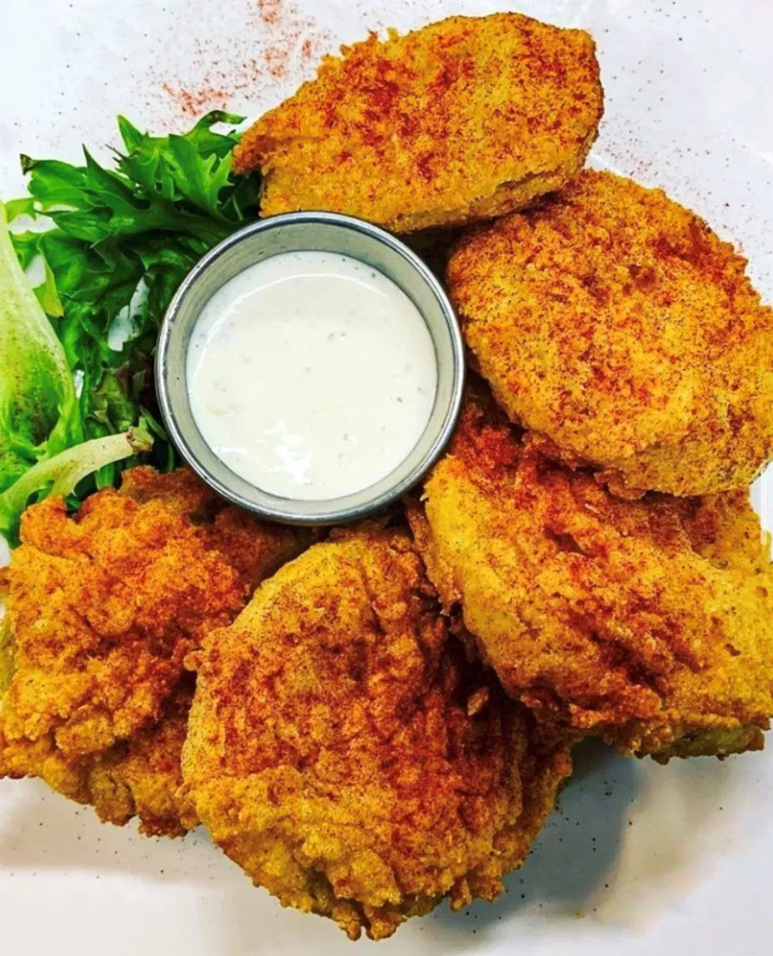 A plate of fried pickles with ranch dressing and lettuce.