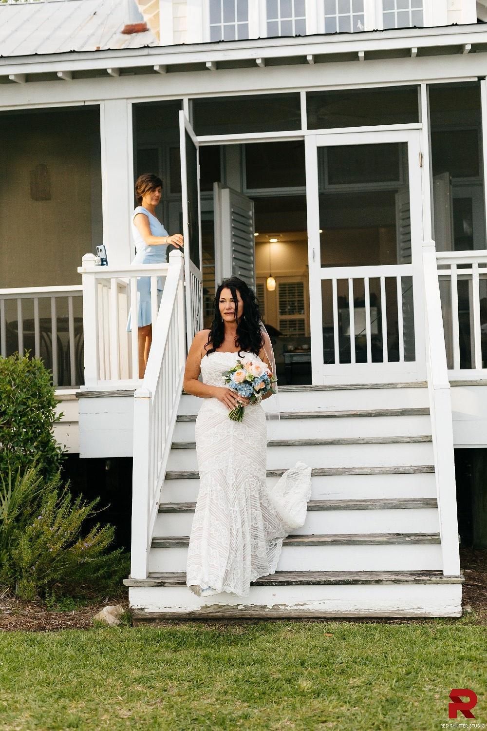 A bride is walking down the stairs of a house holding a bouquet of flowers.
