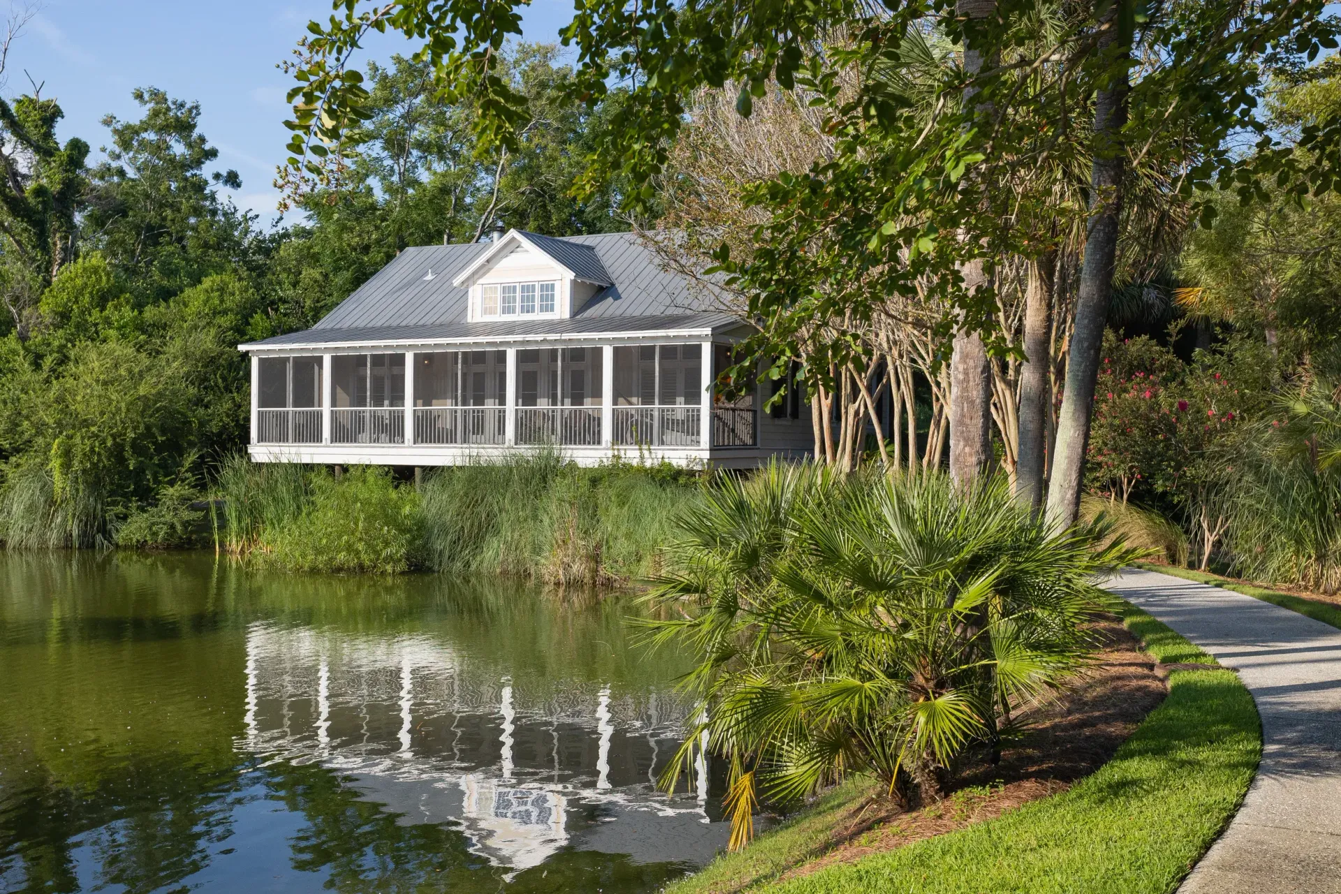 A house with a screened in porch sits next to a lagon surrounded by trees.