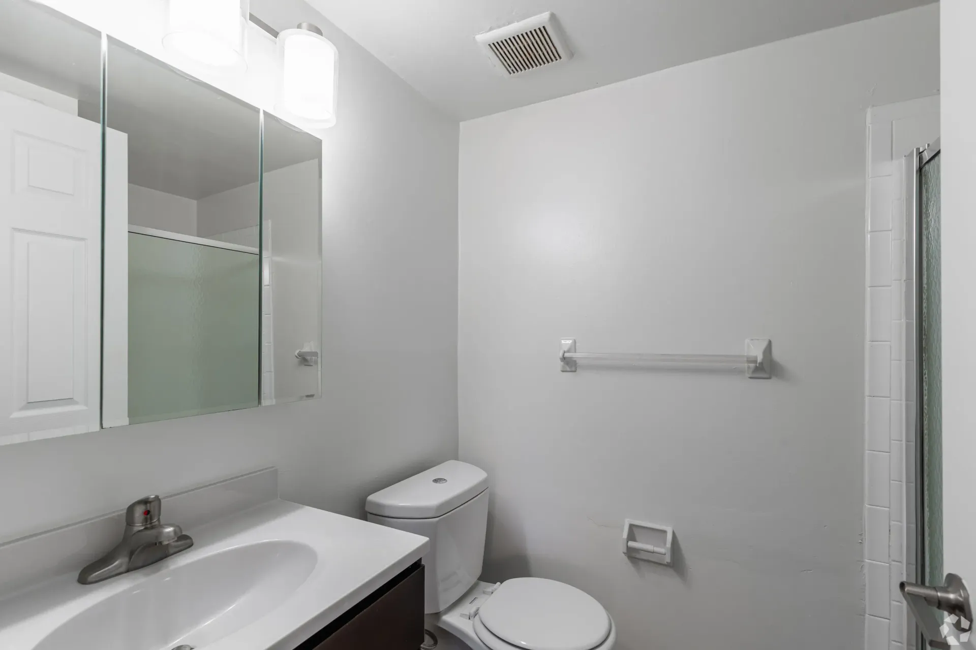 Bathroom in a modern apartment with sink, medicine cabinet mirror, toilet, and shower at Liberty Pointe in Newark, DE.