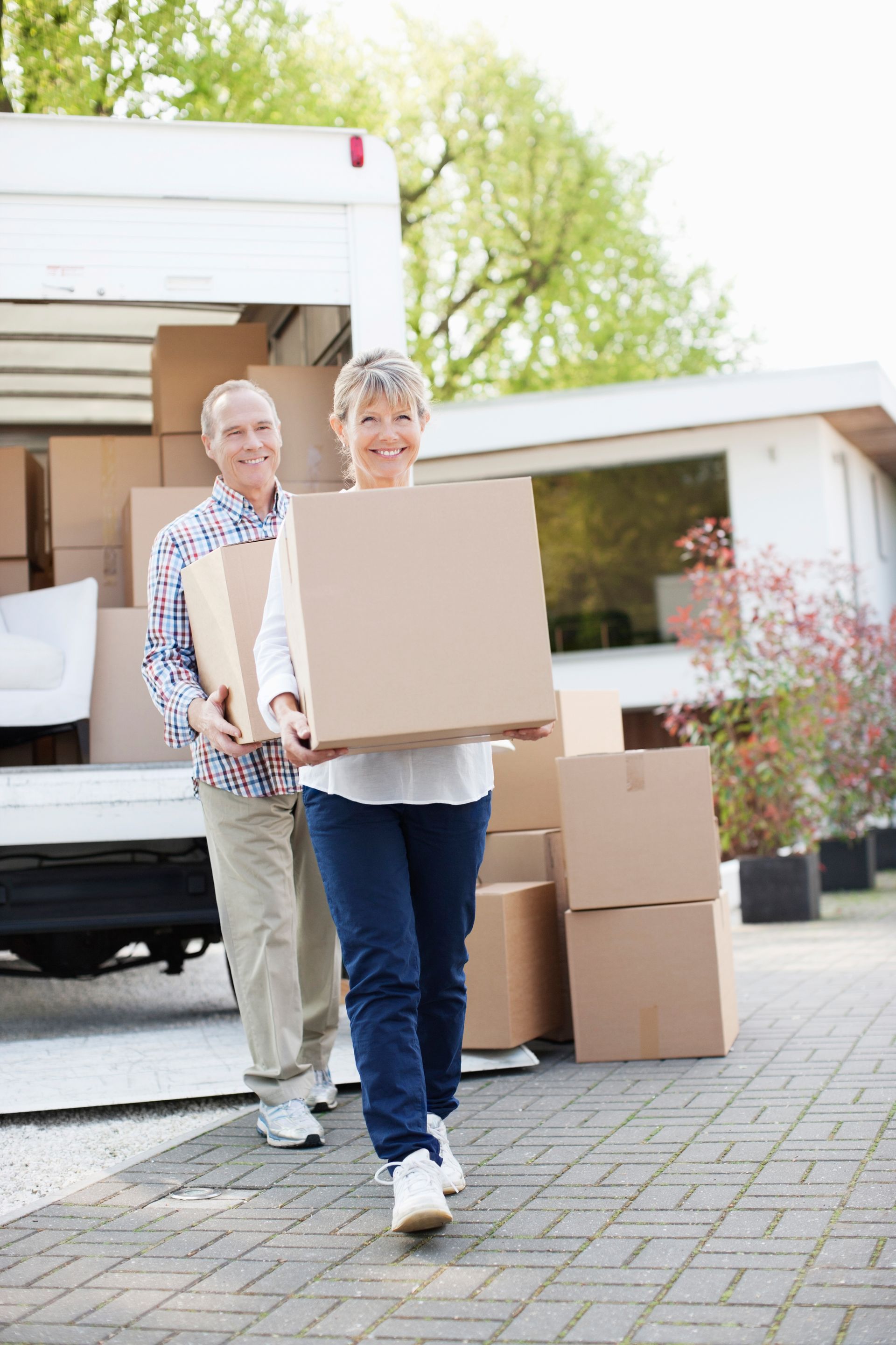 Two people carrying a cardboard box out of a moving truck with stacked boxes nearby