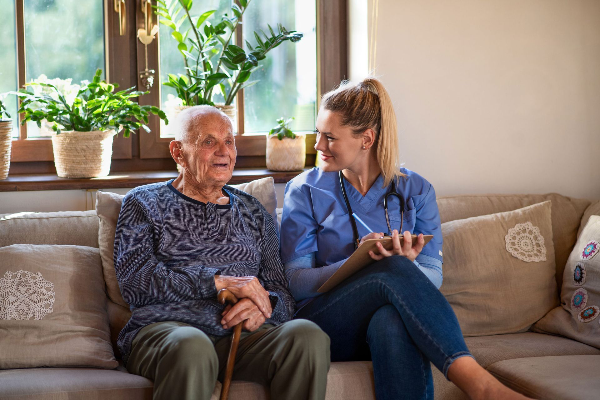 An elderly woman is sitting on a couch with a nurse.