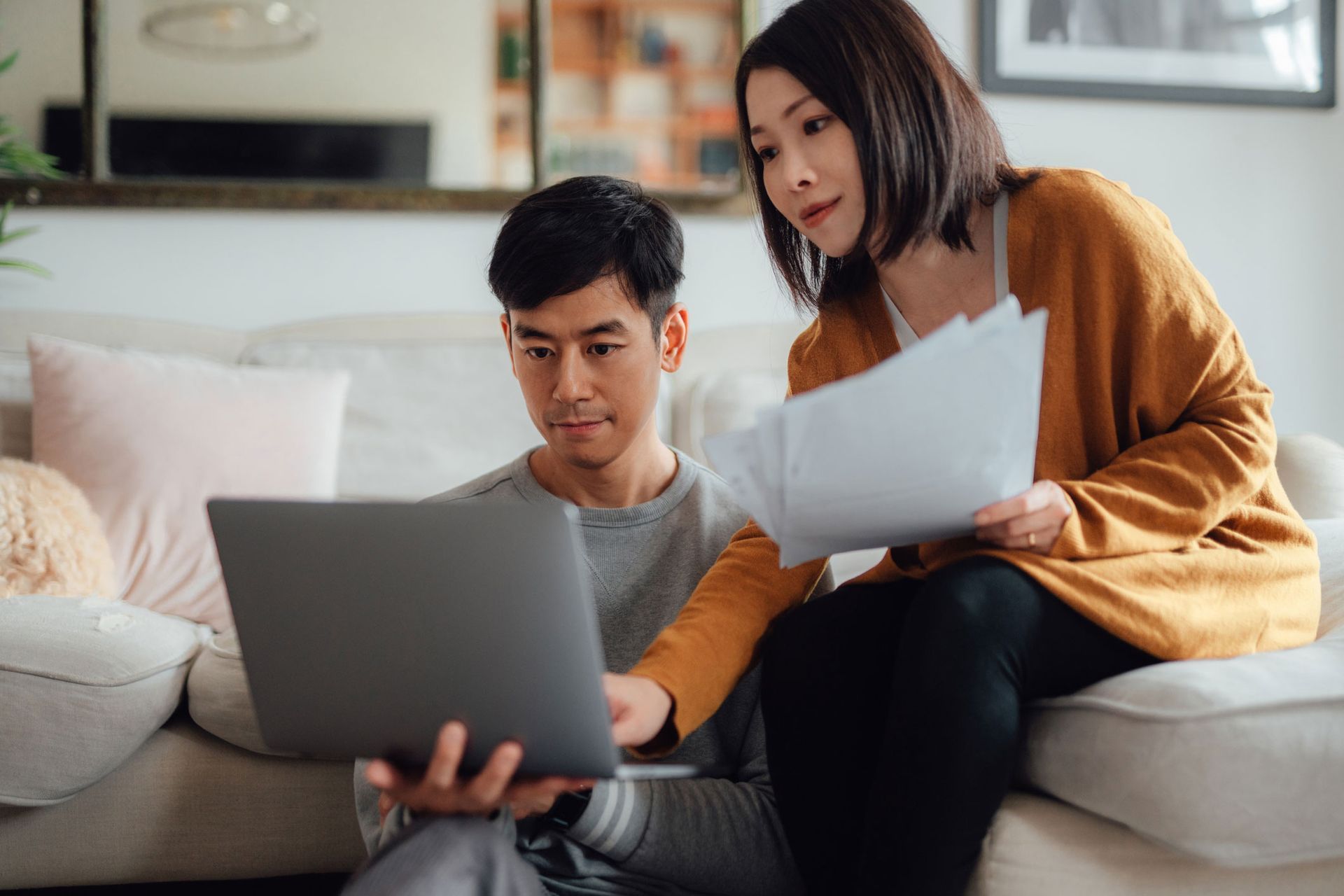 A man and a woman are sitting on a couch looking at a laptop.