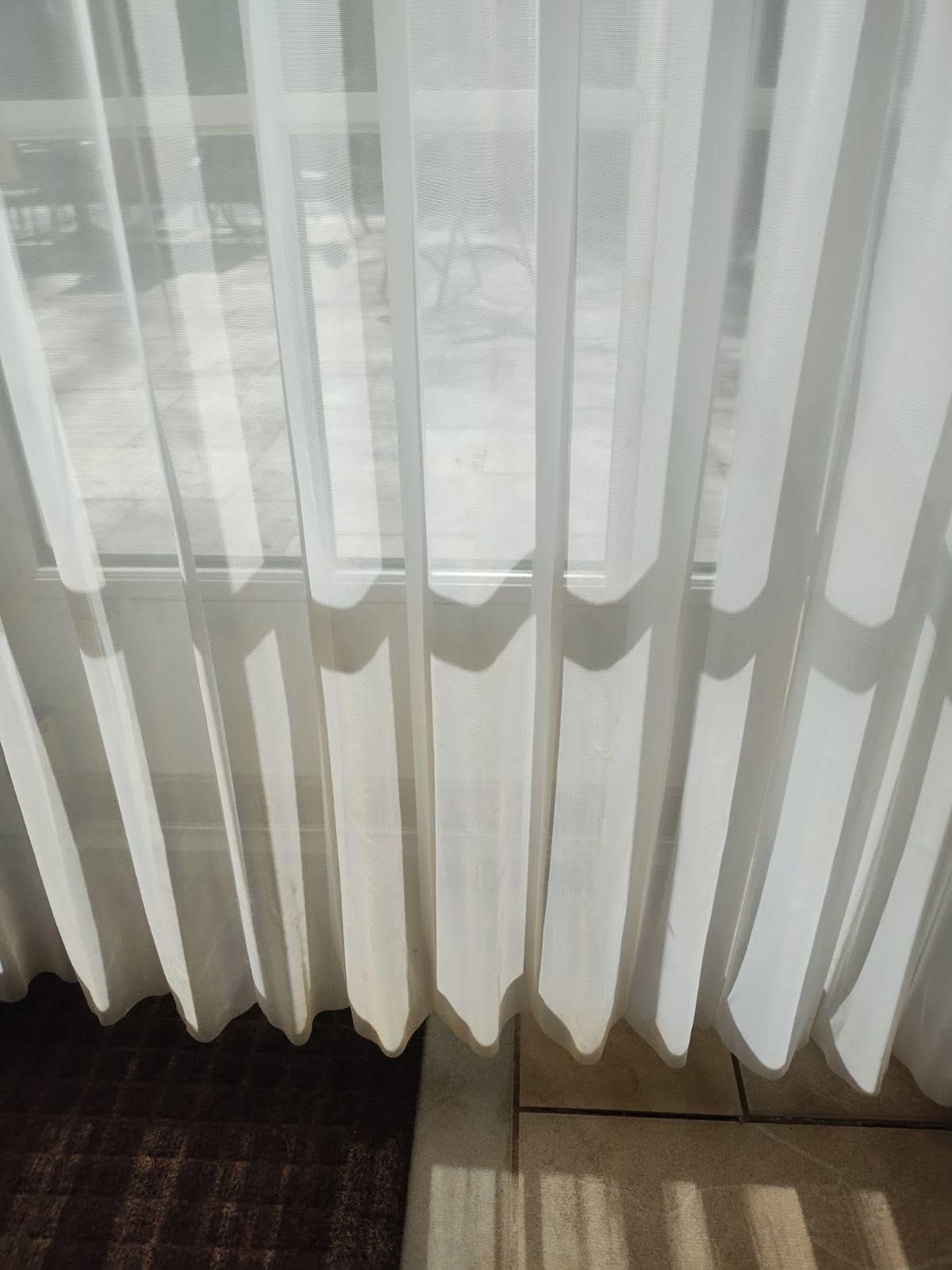 Sheer white curtains filtering daylight over a window above a dark carpet and tiled floor