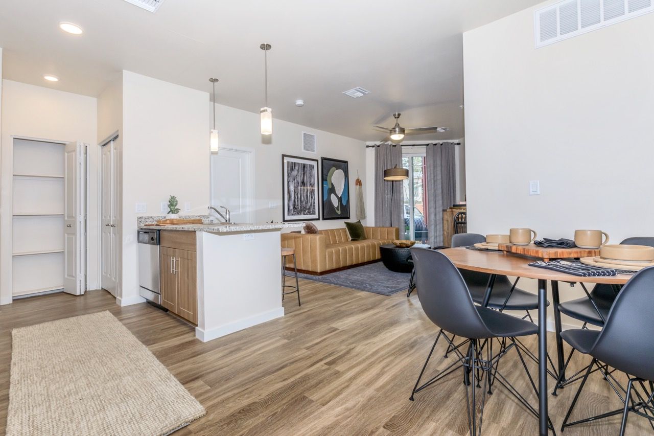 Open-concept apartment living area with kitchen island, pendant lights, tan sofa, dining table, and artwork.