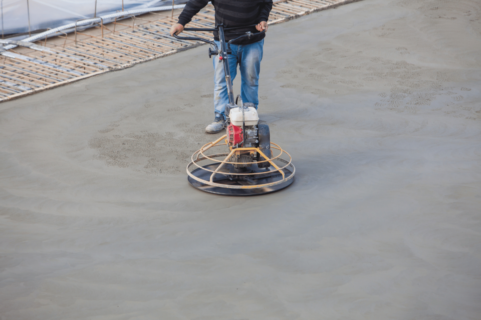 Worker operating a power trowel to smooth wet concrete on a construction site