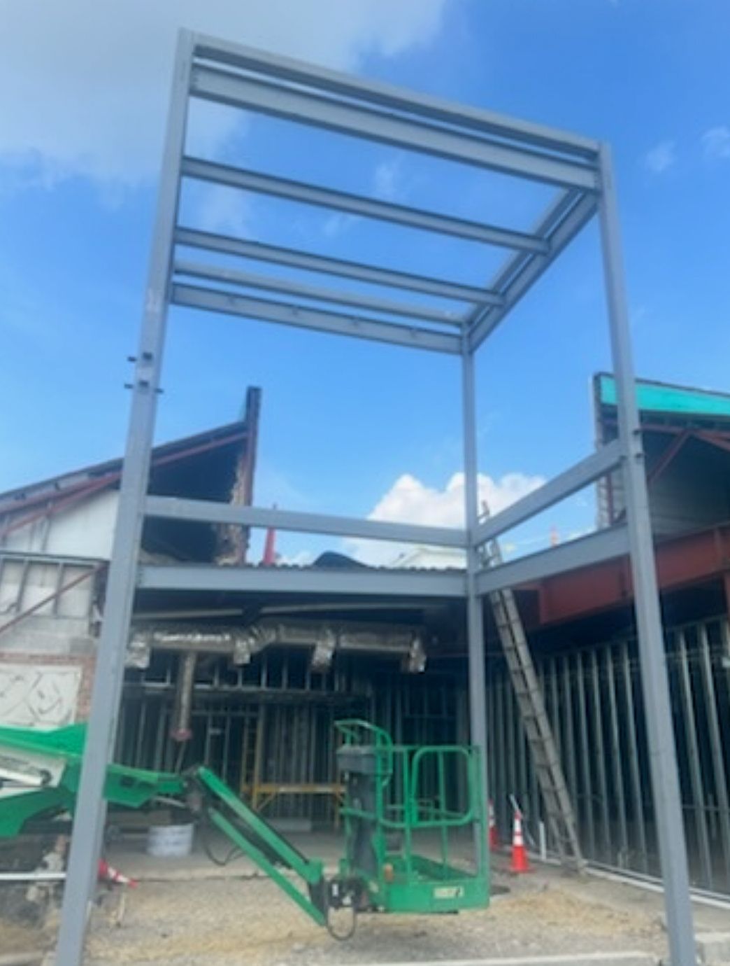 Metal canopy frame under construction beside a green cherry picker in an outdoor worksite