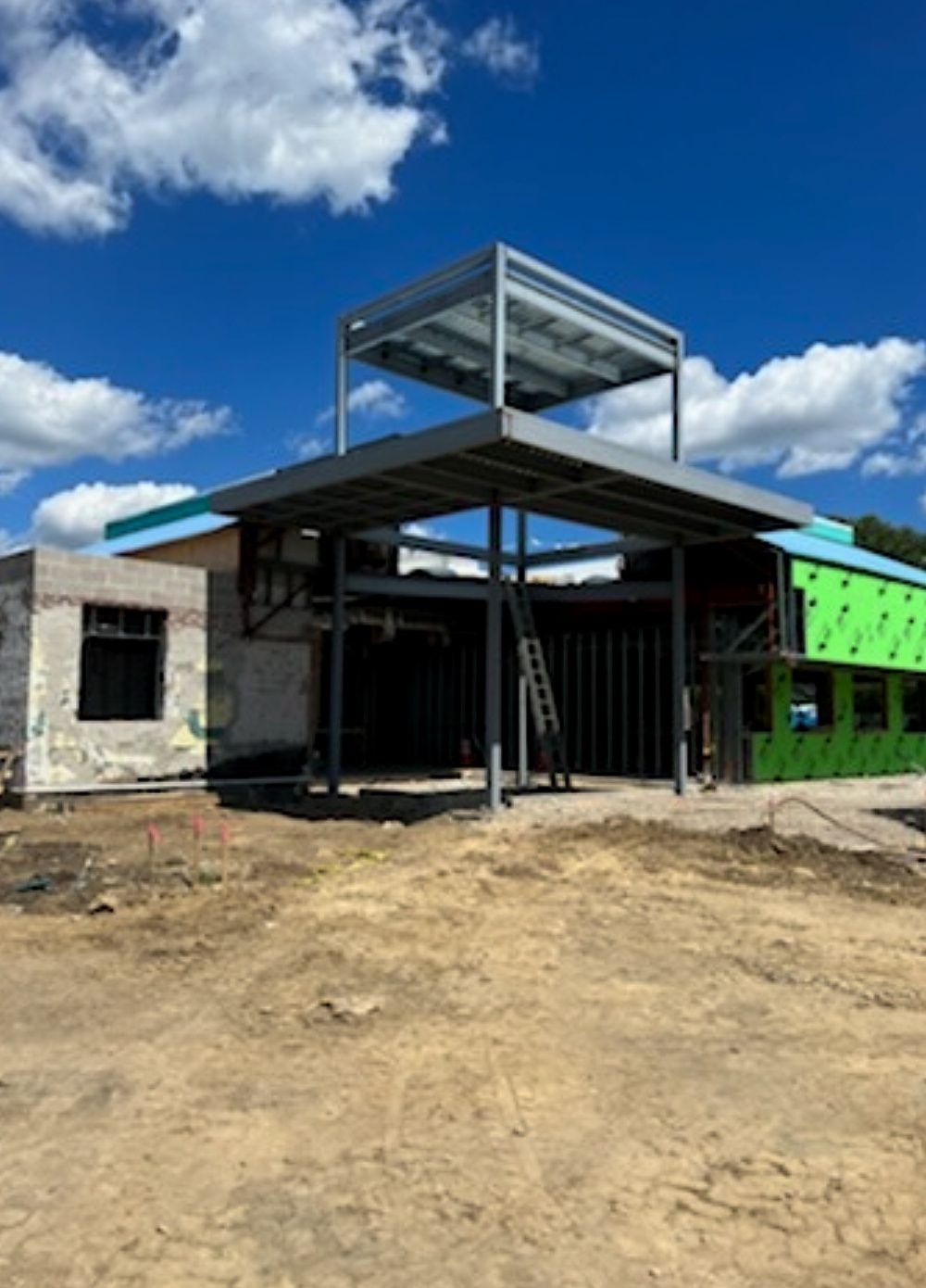 Partially built modern house with exposed framing, gray roof, and bright green side wall under a blue sky