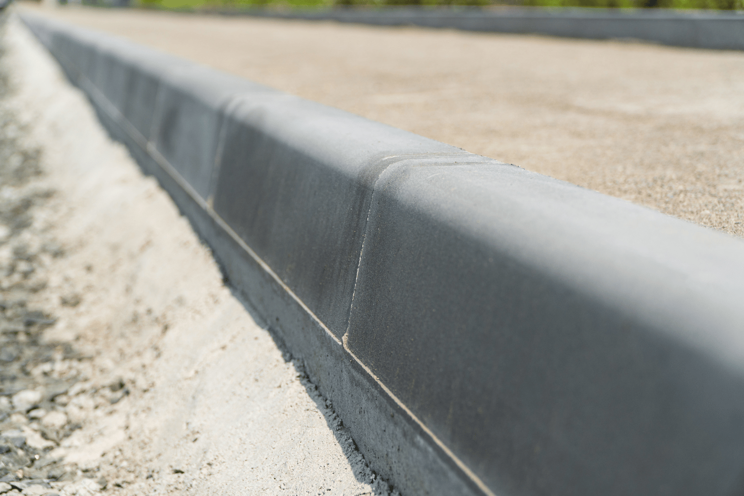 Close-up of a gray concrete curb edging a gravel path beside a paved surface