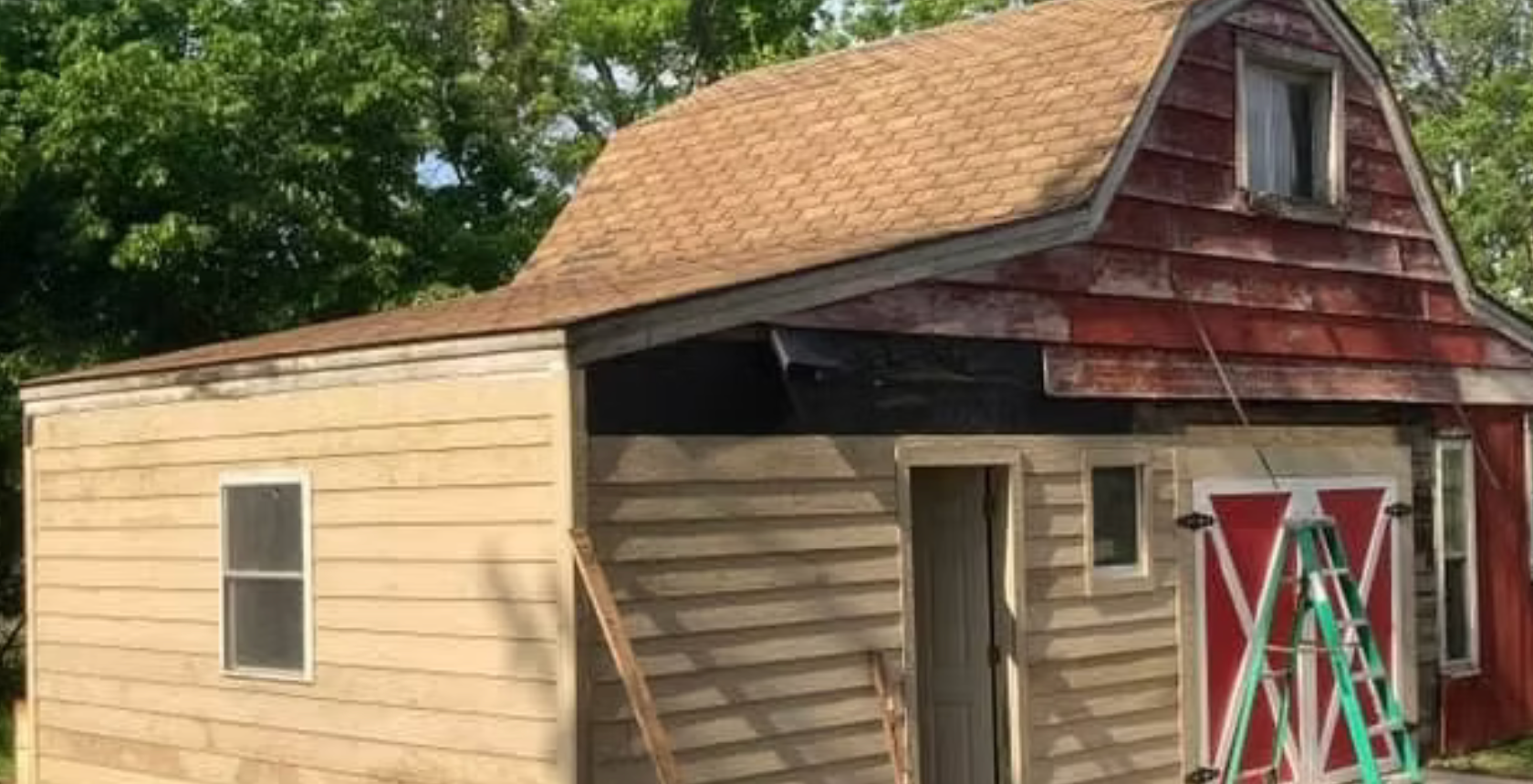Small tan shed with a red roof and open front door, surrounded by trees and a ladder in front.