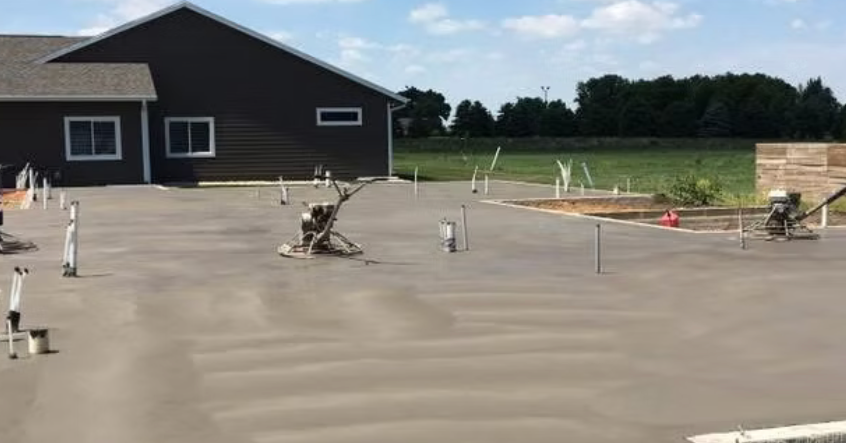 New concrete slab at a house construction site with utility pipes and a dark building in the background