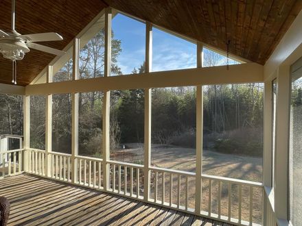 Sunroom with vaulted wood ceiling, tall windows, and a white railing overlooking a sunny yard.