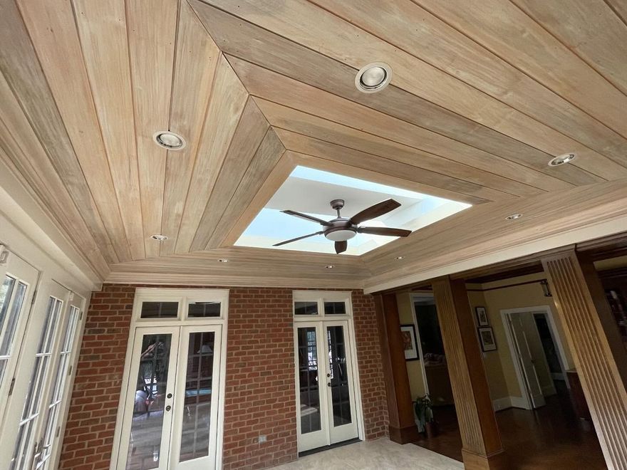Covered brick porch with wood-paneled ceiling, ceiling fan, and white French doors