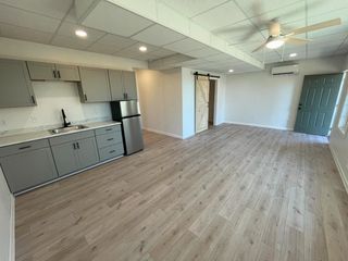 Empty open-concept room with gray kitchen, wood-look floors, white walls, and ceiling fan