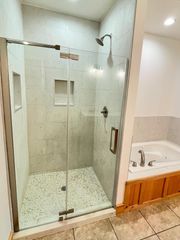 Glass walk-in shower beside a white vanity with wood cabinets in a tiled bathroom