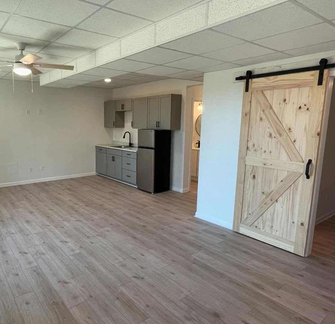 Empty room with wood-look flooring, ceiling fan, kitchenette, and barn-style sliding door