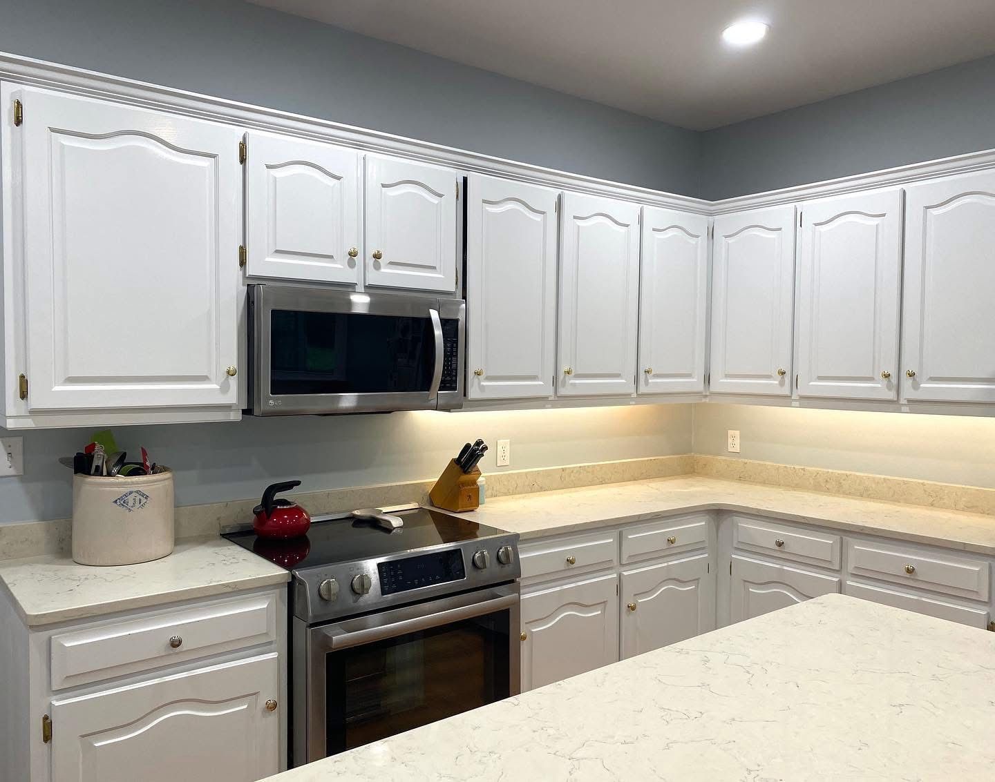 Bright white kitchen with white cabinets, stainless oven and microwave, under-cabinet lighting, and a pale countertop.