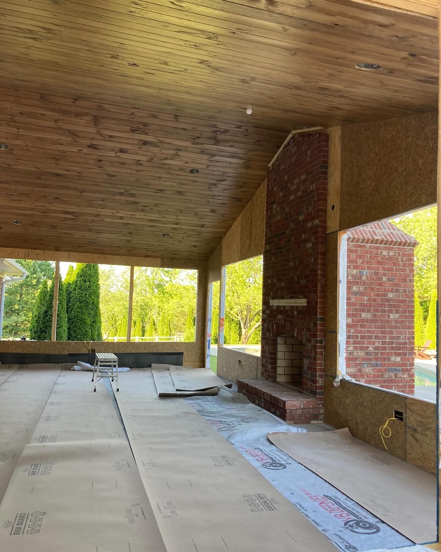 Covered porch under construction with brick column, wood ceiling, and insulation on the floor