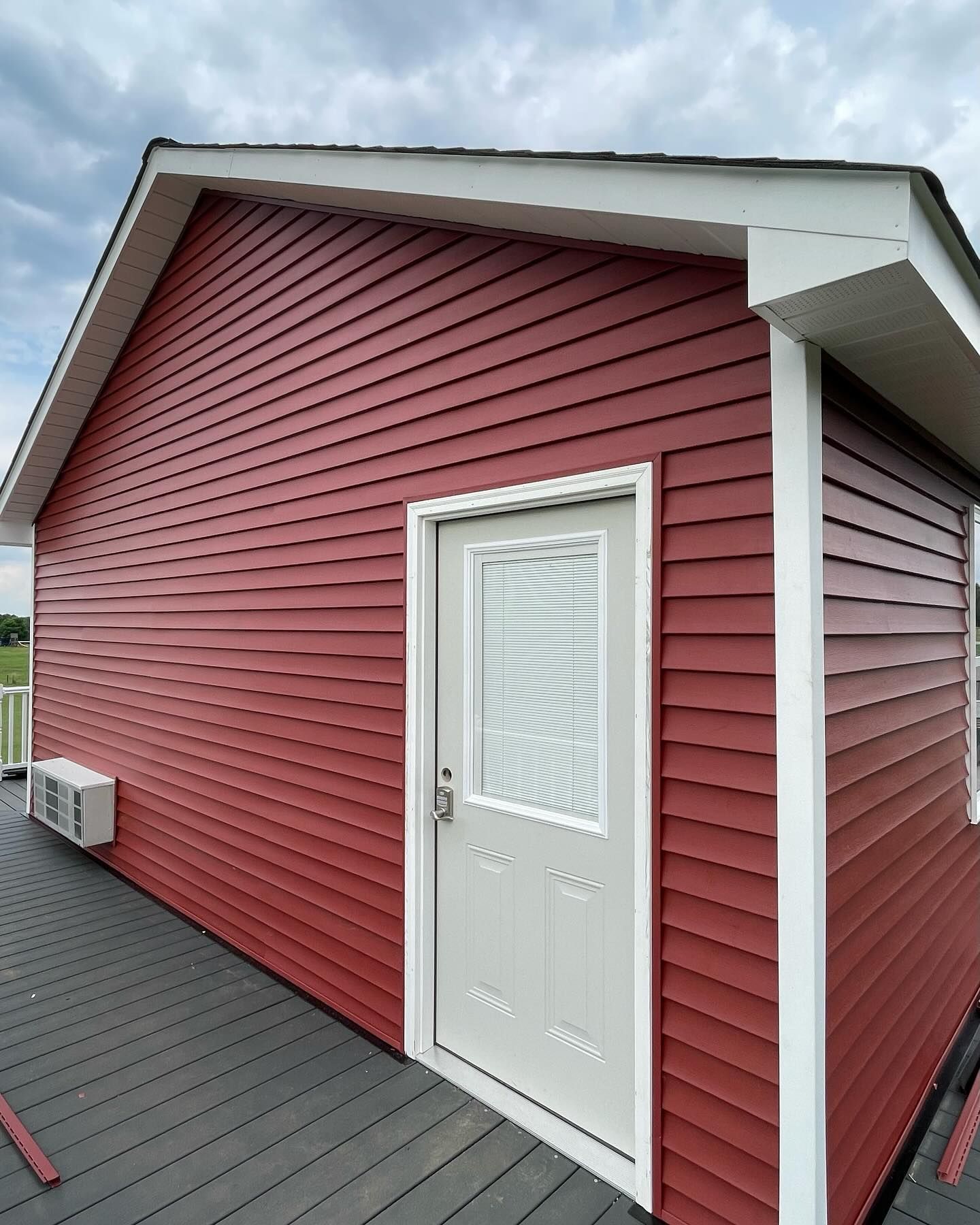Red-sided building exterior with white door and small wall-mounted AC unit on a gray deck.