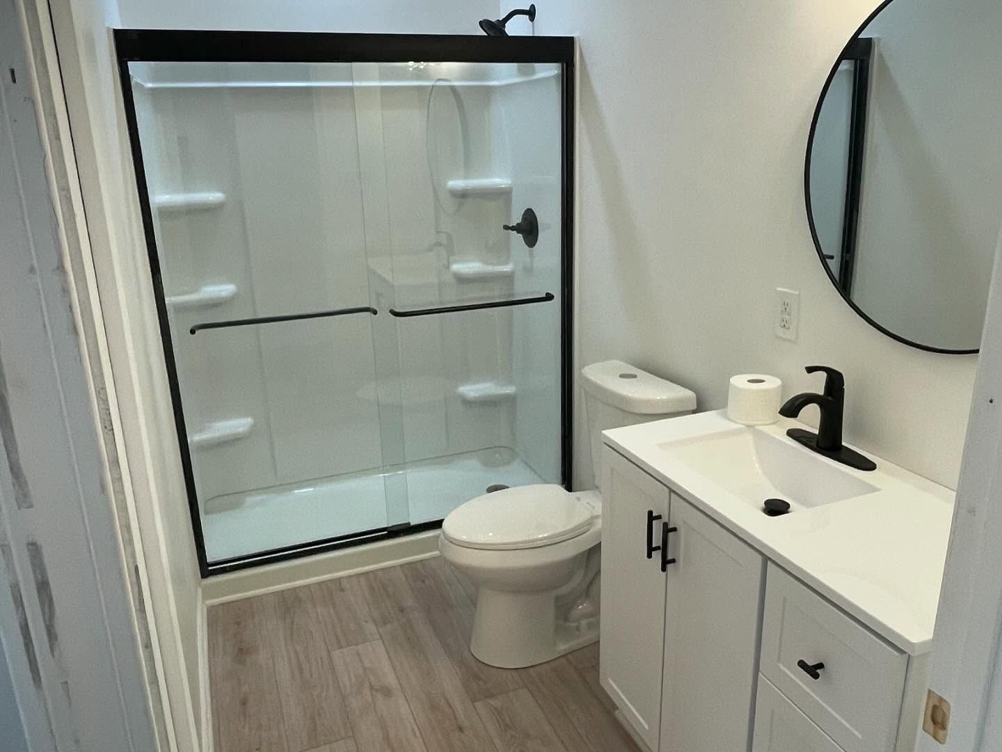 Modern bathroom with glass shower, toilet, vanity sink, and round wall mirror