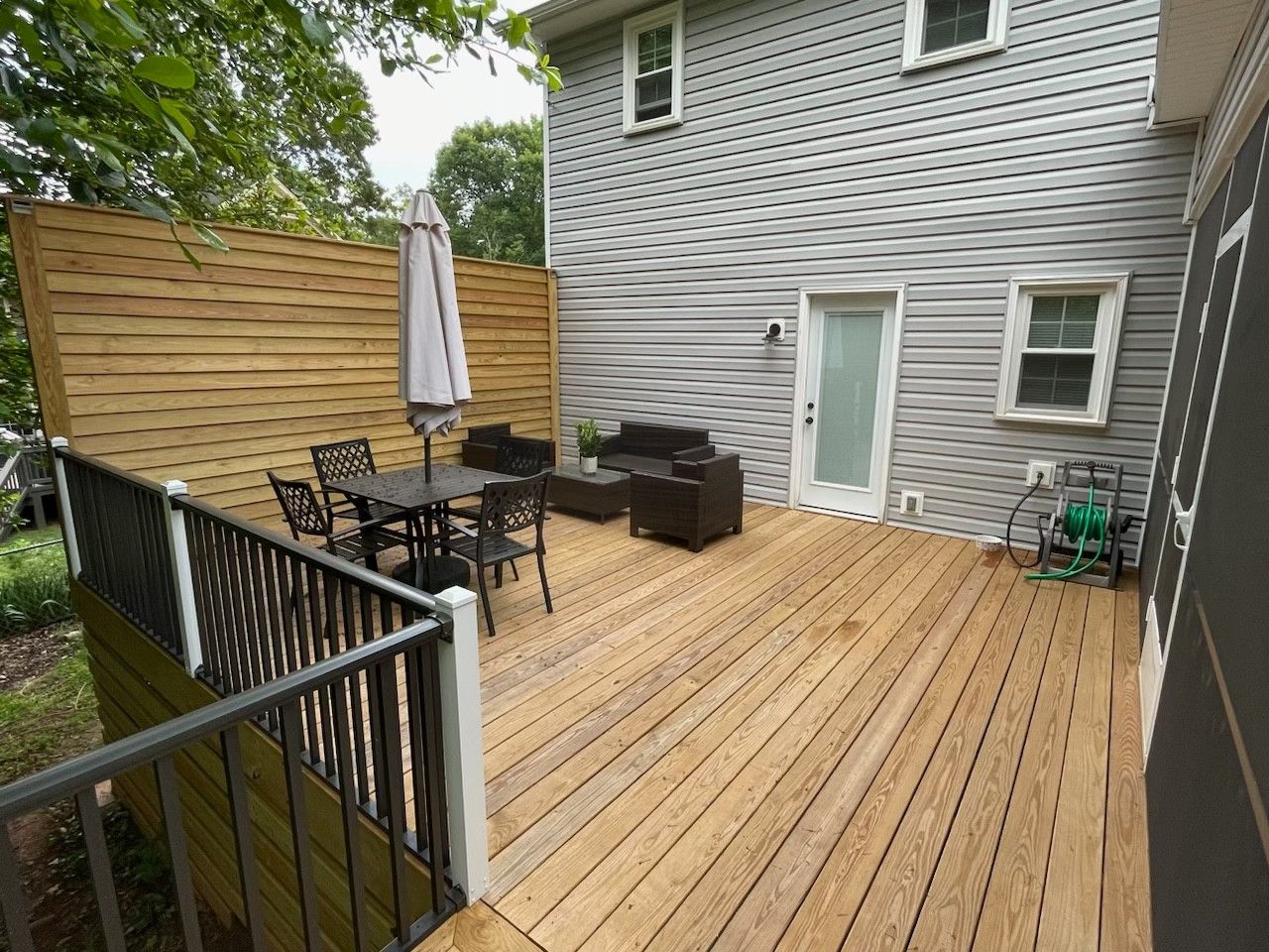 Wooden backyard deck with patio table, chairs, umbrella, and gray house exterior.