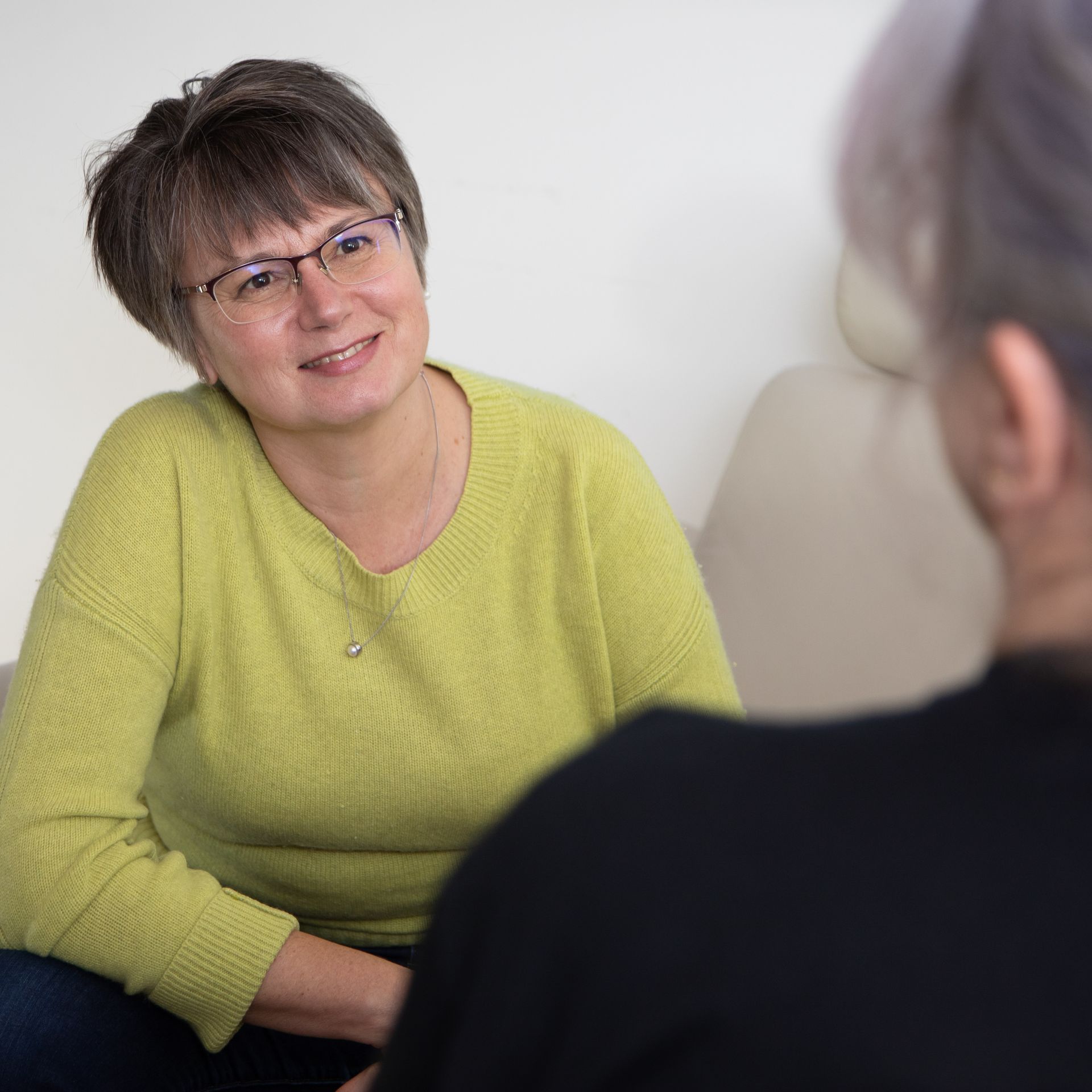 Two people talking in a bright room, one smiling in a lime-green sweater.