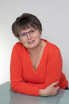 Person in a bright orange top leaning on a table, smiling at the camera.