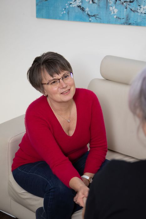 Woman in red sweater seated on a couch, smiling and leaning forward in conversation.