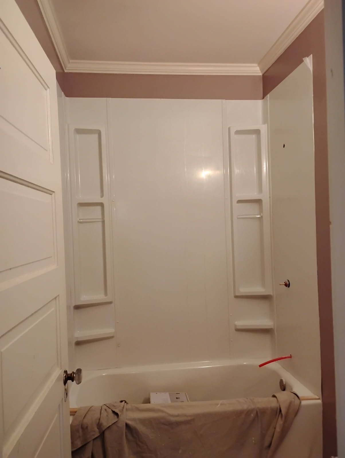 Empty bathroom with a white tub, built-in shelves, and a brown towel draped over the tub edge