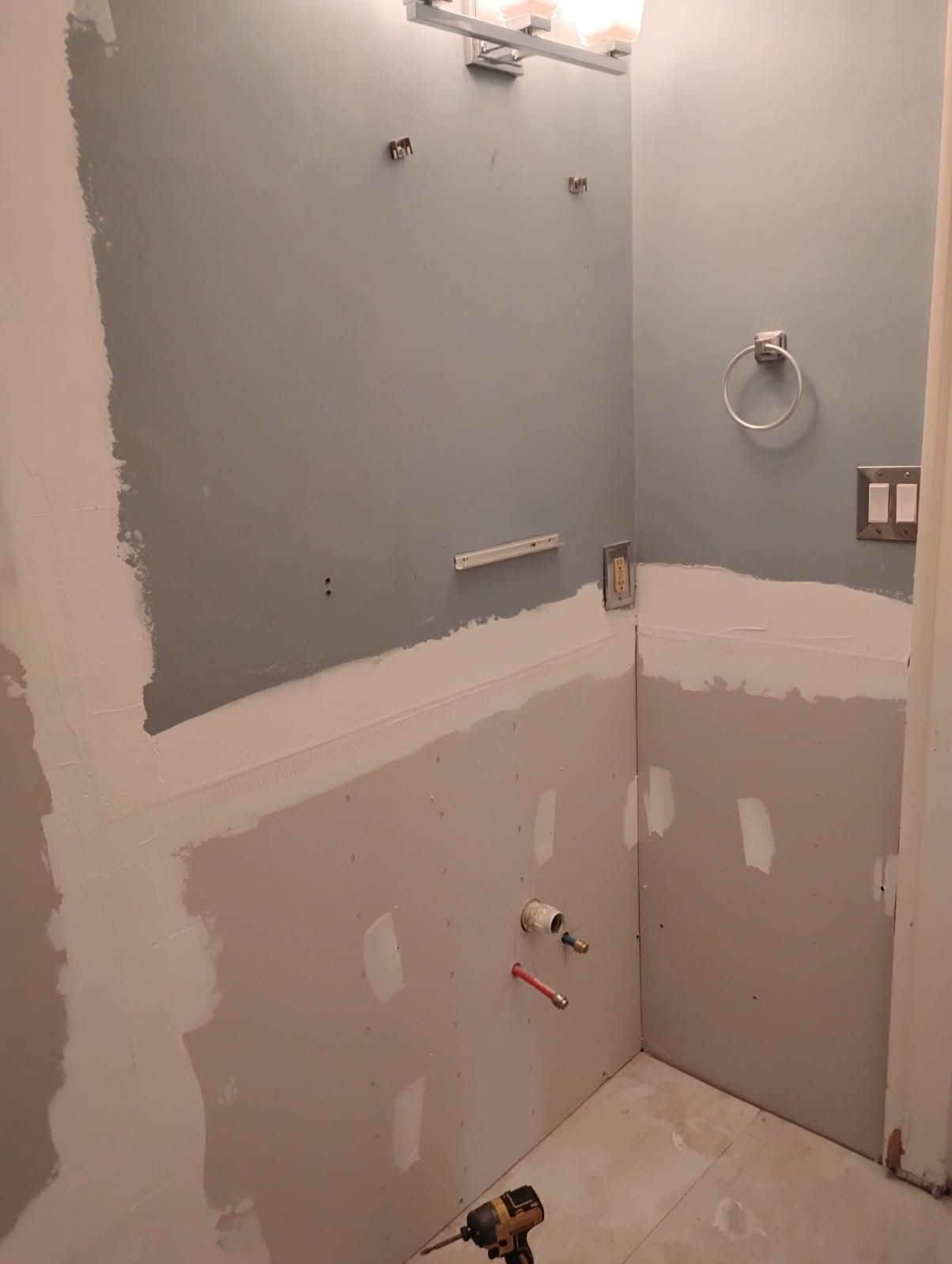 Unfinished bathroom wall with gray drywall patches, exposed plumbing, and a towel ring.
