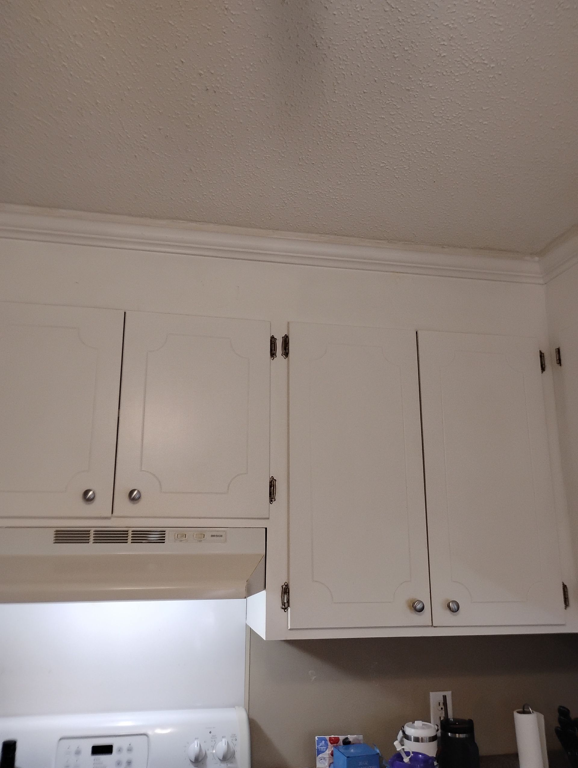 White kitchen cabinets installed against a textured white ceiling, situated above a stove and kitchen counter.