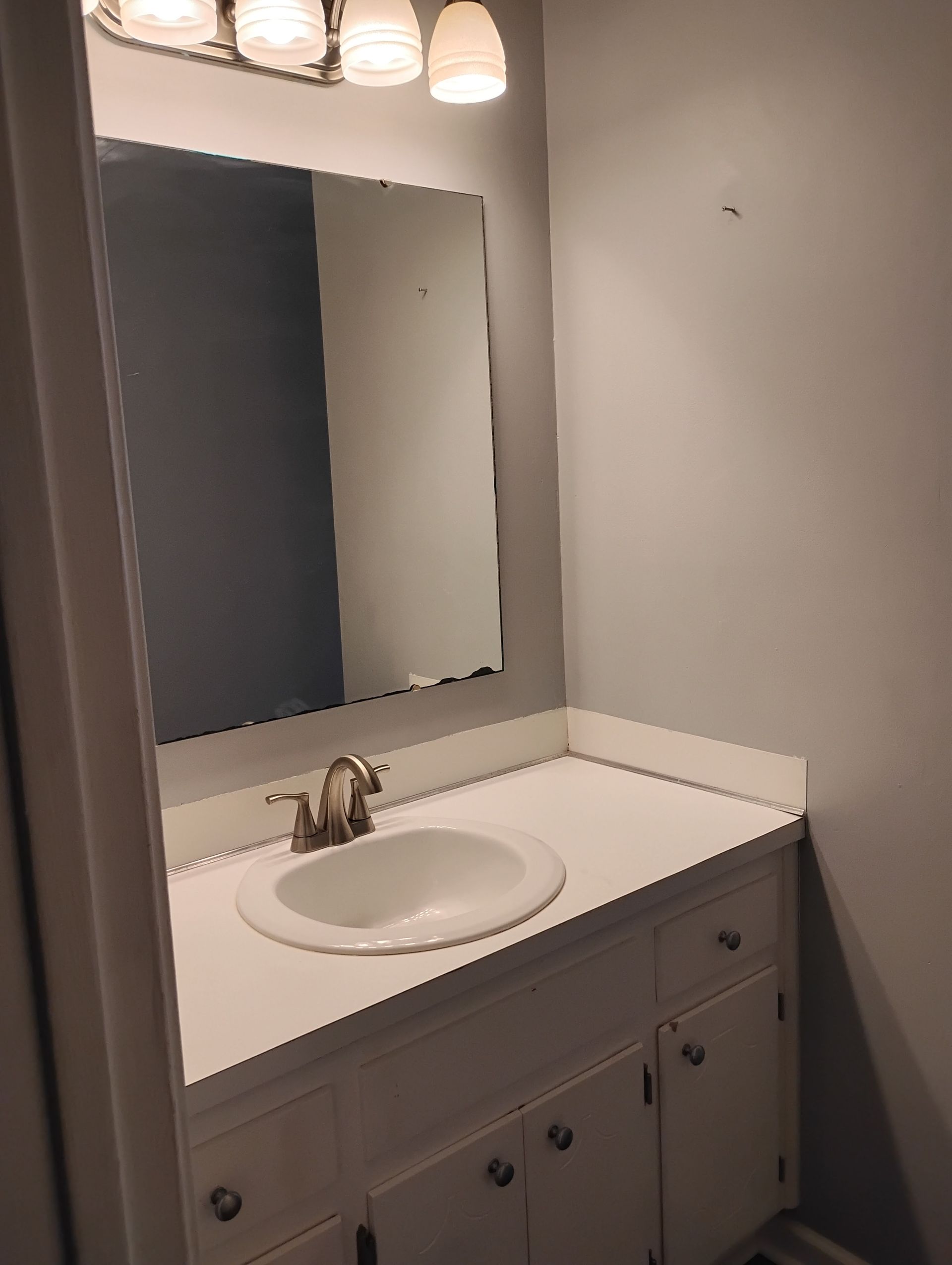 A bathroom vanity with a white countertop and sink, a faucet, a wall mirror, and a four-light fixture above it.