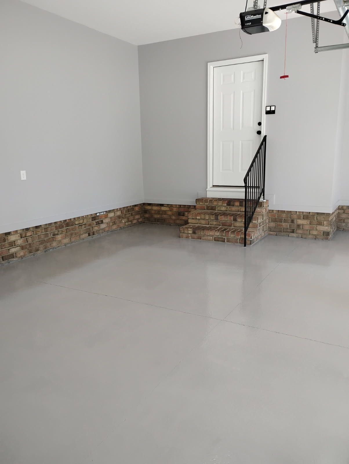 Empty garage with gray walls, stone trim, and a white door with steps and a black handrail