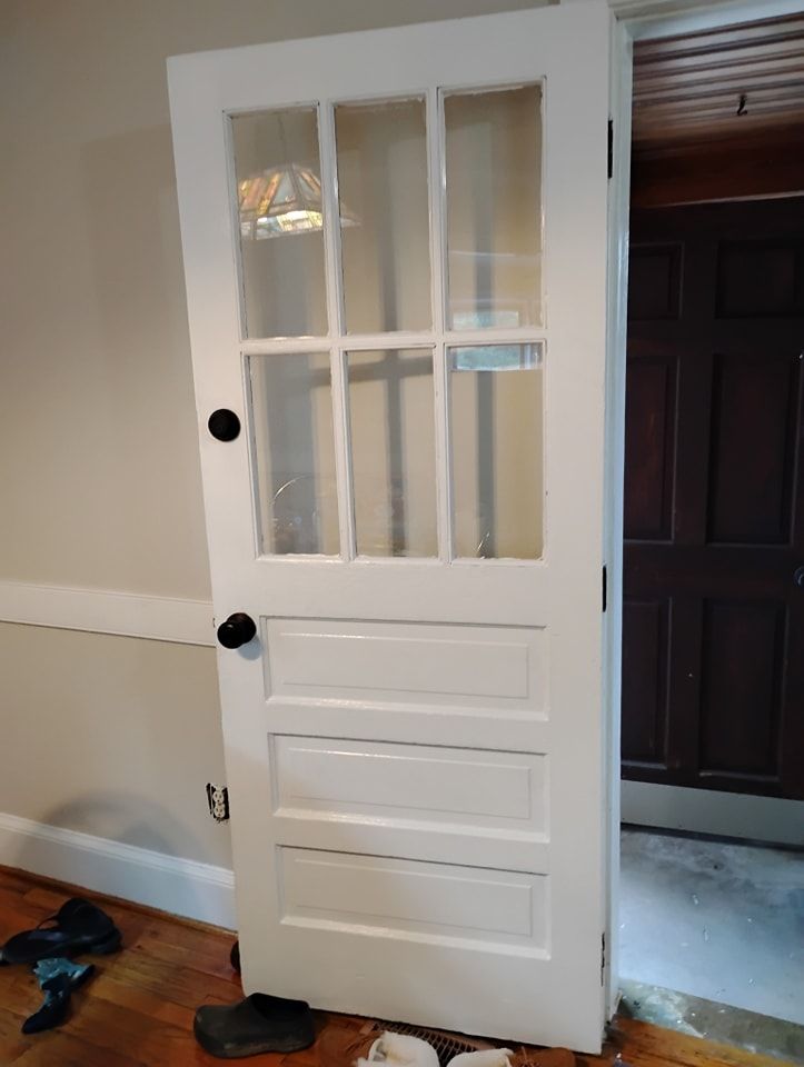 A white wooden door with six glass window panes at the top and three rectangular panels below, standing in a room.